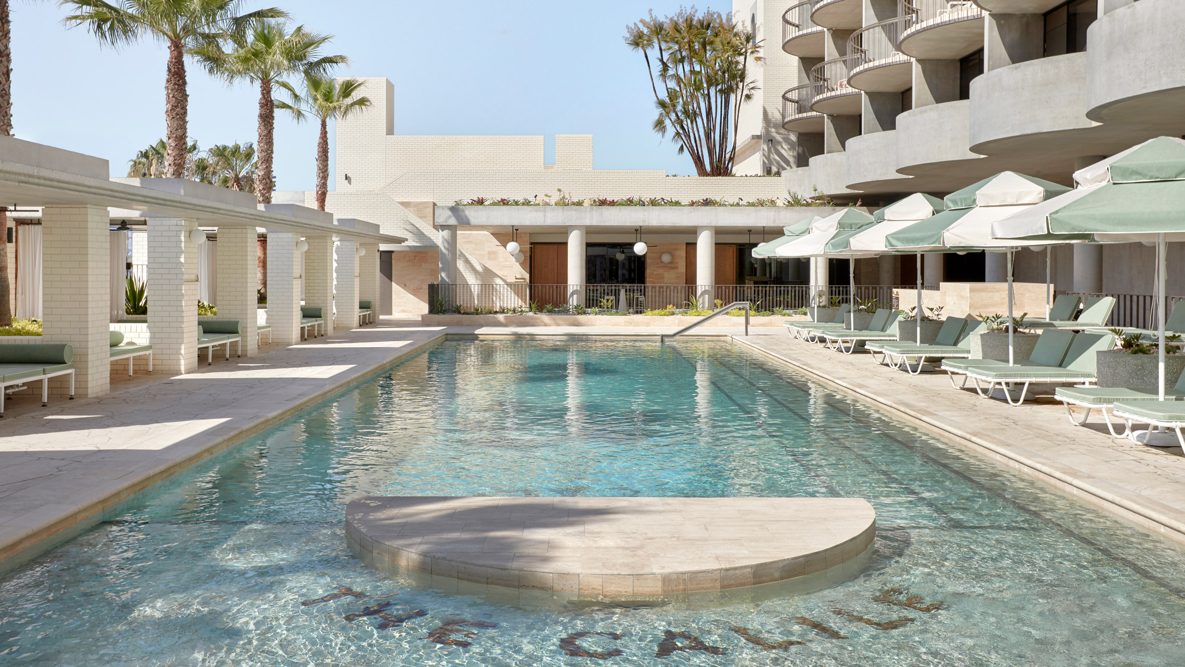 The Calile pool deck with green-cushioned cabanas, the curved hotel facade behind.